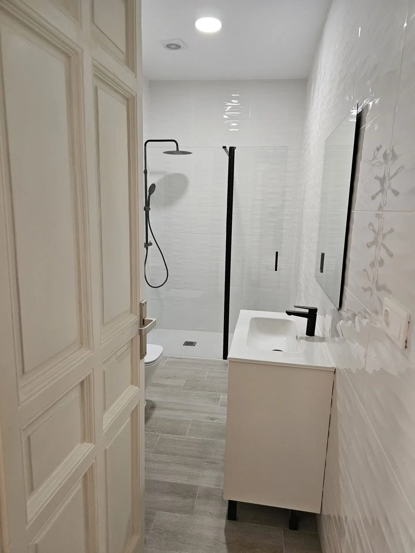 Baño reformado con ducha de mampara, grifería negra, mueble de lavabo y azulejos blancos