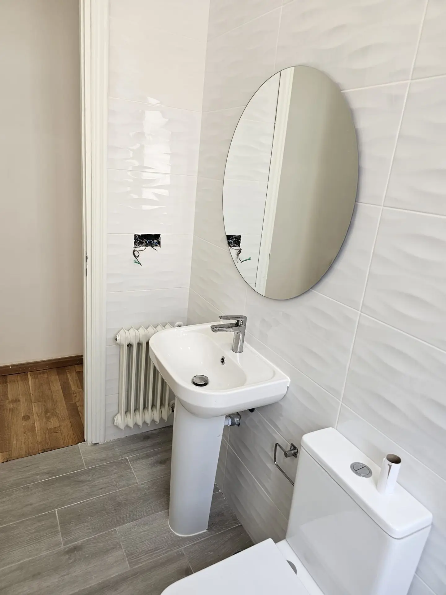 Lavabo blanco con espejo redondo y radiador toallero en un baño reformado