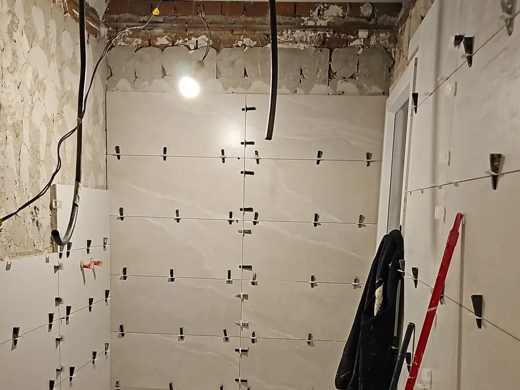 Pared con azulejos blancos y crucetas de nivelación durante el alicatado de una reforma integral