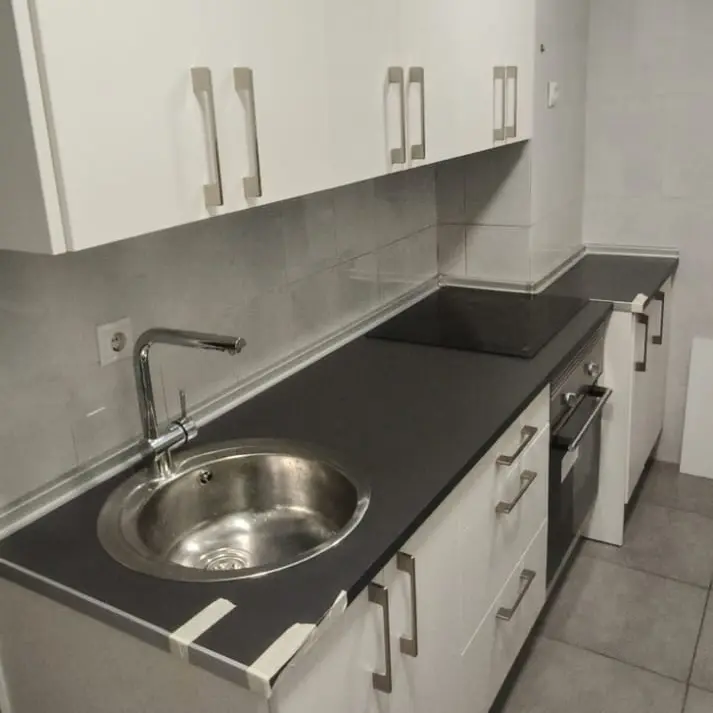 Fregadero de acero inoxidable en una cocina reformada con muebles blancos y encimera negra