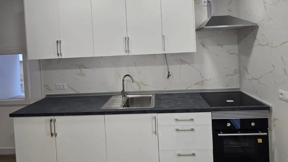 Cocina terminada con muebles blancos, encimera negra, fregadero, campana y horno