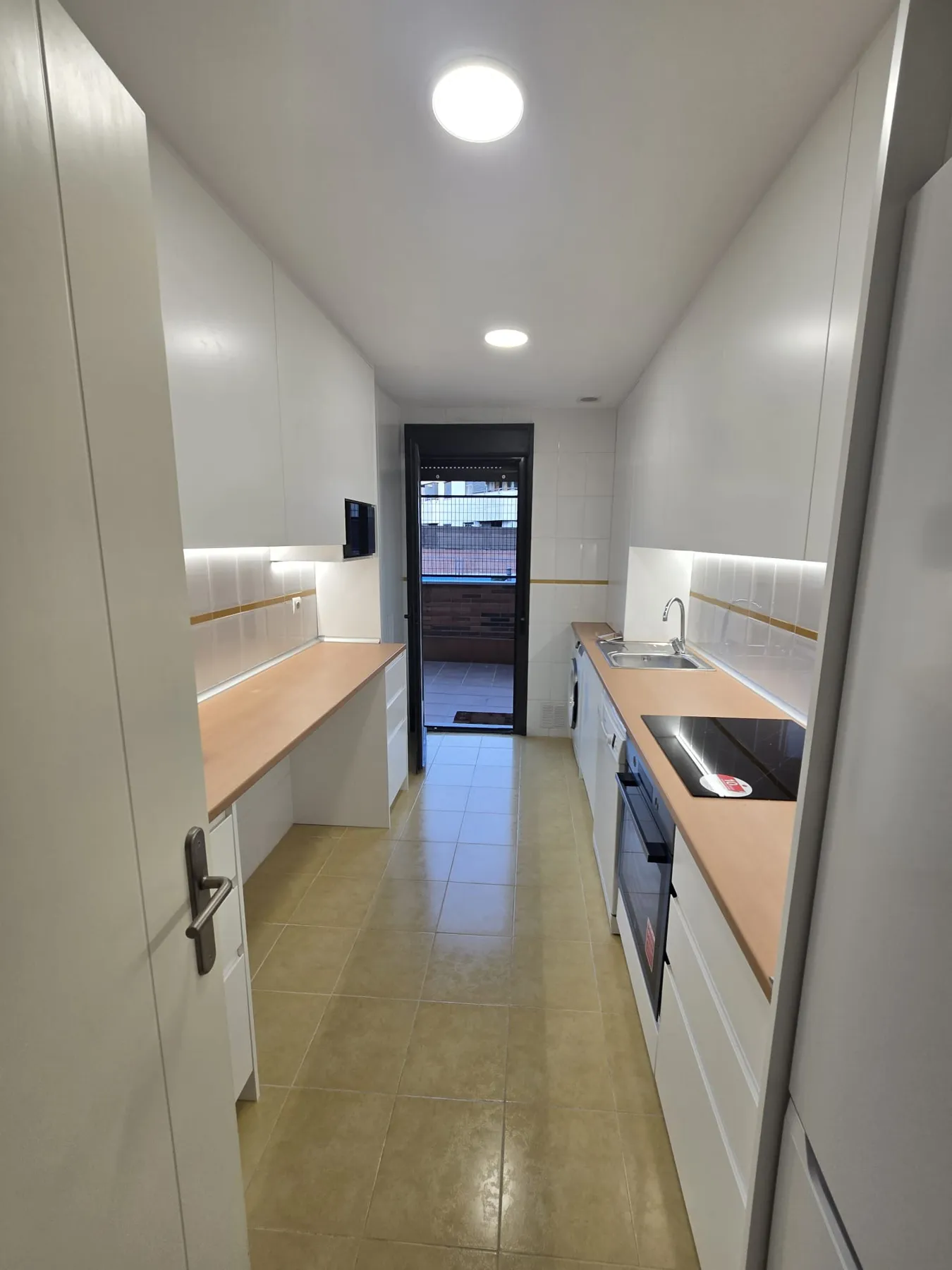 Cocina reformada con muebles blancos, encimera de madera y puerta a la terraza