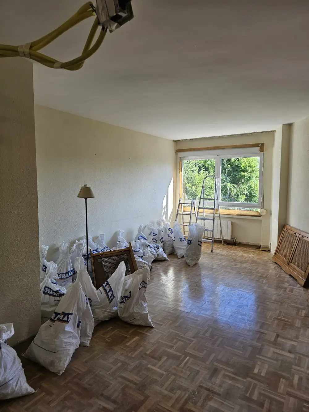 Salón de una vivienda en obra durante una reforma integral, con sacos de escombro y escaleras
