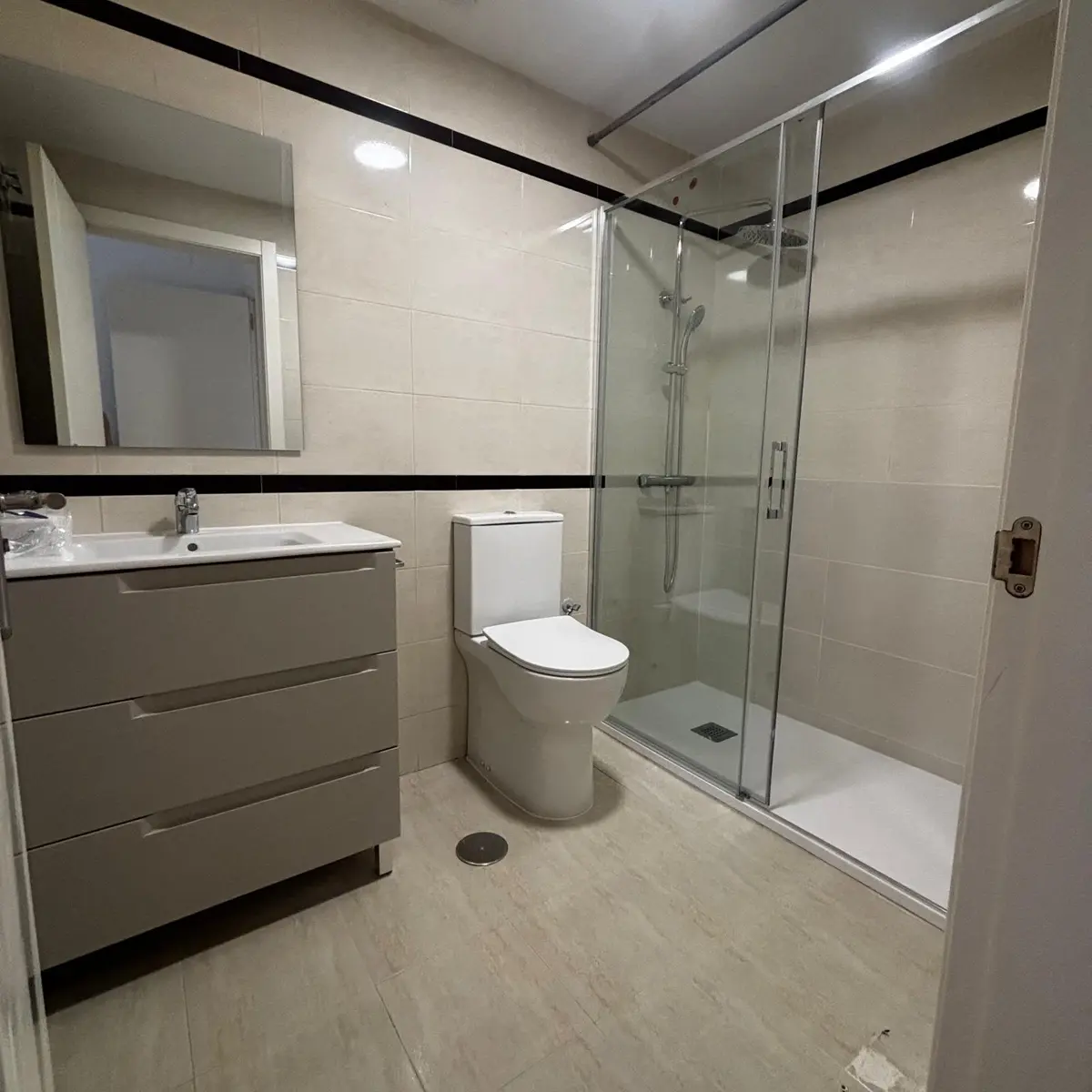 Baño reformado con mueble de lavabo, inodoro y ducha con mampara de cristal